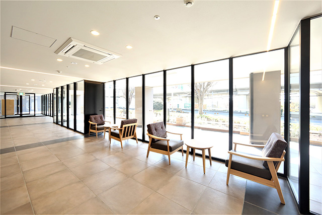 Glass-walled entrance hall, filled with natural lighting. The window frames, flush door and the automatic entrance door frames are Kikukawa metals.